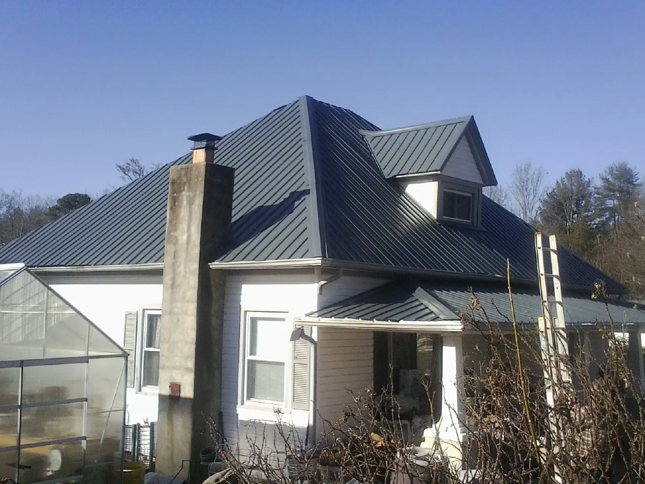 Dark blue standing seam metal roof on a white farmhouse with dormer — Slate & Tile Roof Repair by Roofing Brothers in Riegelwood