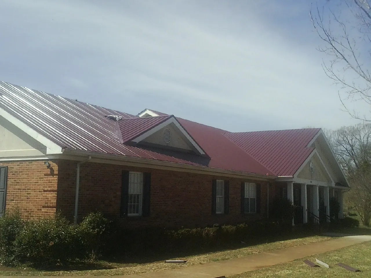Red metal roof with gabled entries on a long brick building, from a Hail Damage Roof Repair job in Riegelwood