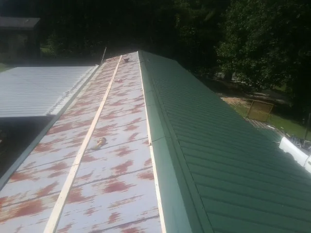 Old rusted panels beside newly installed green metal roofing — Wind Damage Roof Repair by Roofing Brothers in Riegelwood