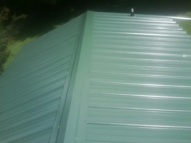 New green metal panels meeting at the ridge of a roof — Flat Roof Repair work by our crew in Riegelwood
