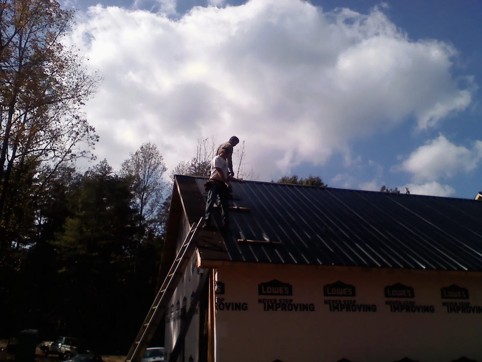 Roofer fastening dark metal panels high against a cloudy sky, from a Roof Inspection job in Riegelwood