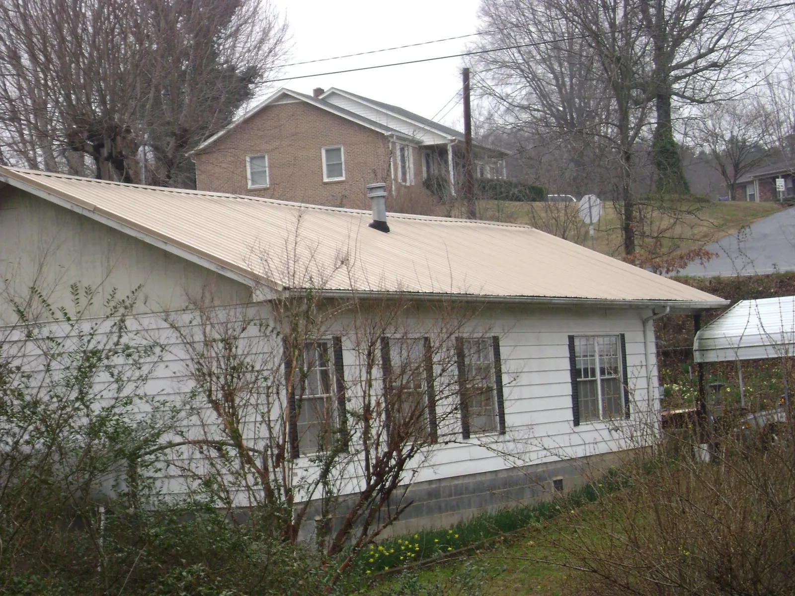 Tan metal roof on a white sided house set into a hillside — Commercial Roofing by Roofing Brothers in Riegelwood