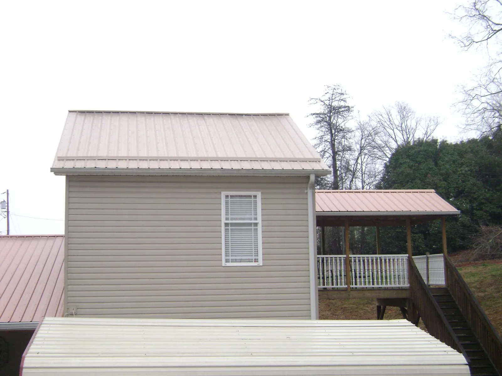 Tan metal roofs on a two story addition and attached porch, from a Roof Replacement job in Riegelwood